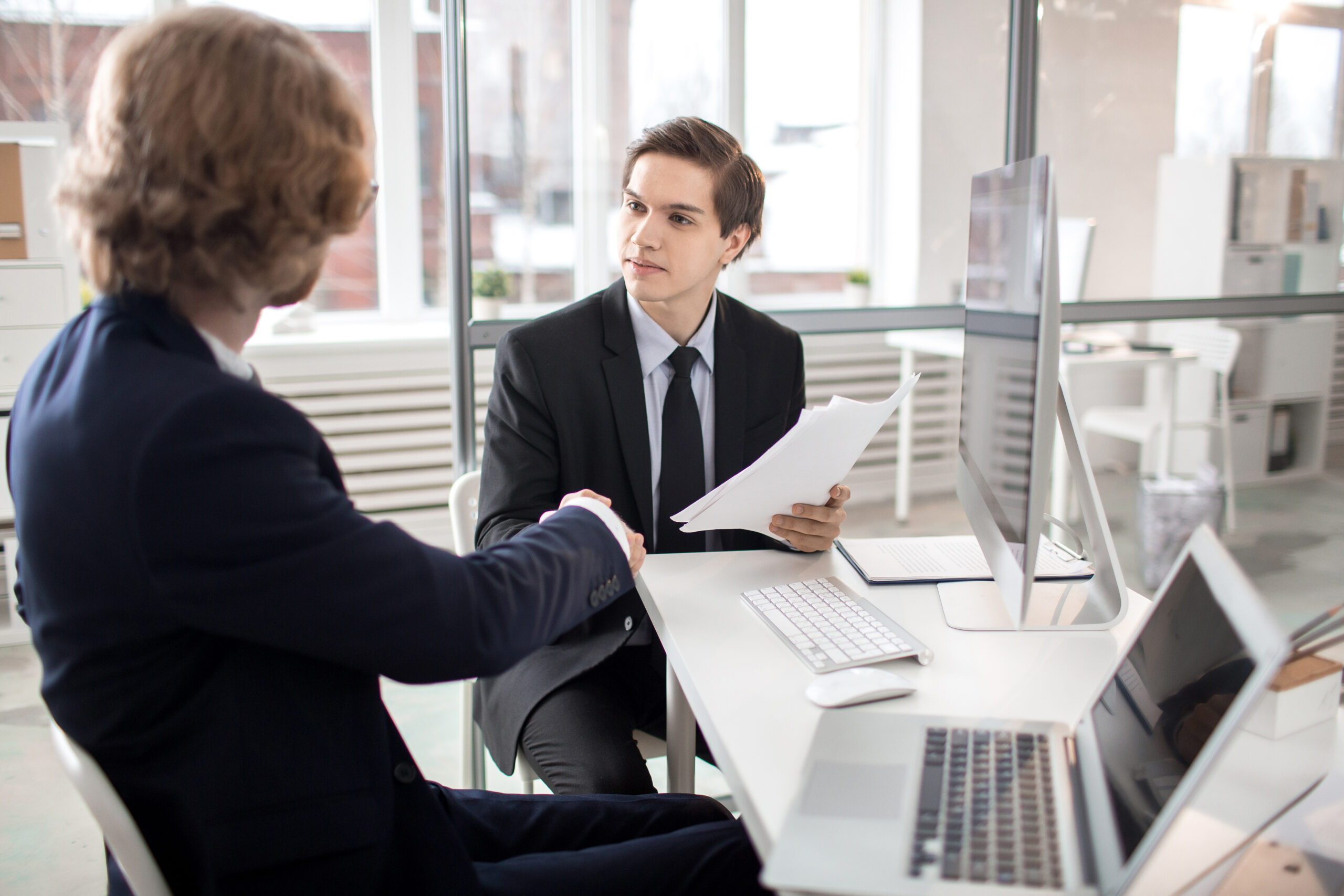 Young business partners handshaking after signing contract in office